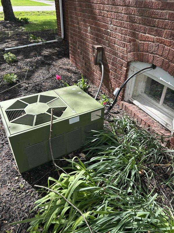 Completed HVAC system replacement estimate and site evaluation following tech lead coordination. Documented existing outdoor condensing unit positioned against brick exterior with refrigerant line set running vertically along building wall. Interior inspection revealed furnace or air handler installation in utility room adjacent to laundry appliances, with proper warning labels present regarding refrigerant connection procedures. Photographed current equipment configuration, line set routing, and installation conditions to support replacement proposal. System assessment included evaluation of outdoor unit placement in landscaped area and interior mechanical space constraints for new equipment installation planning.