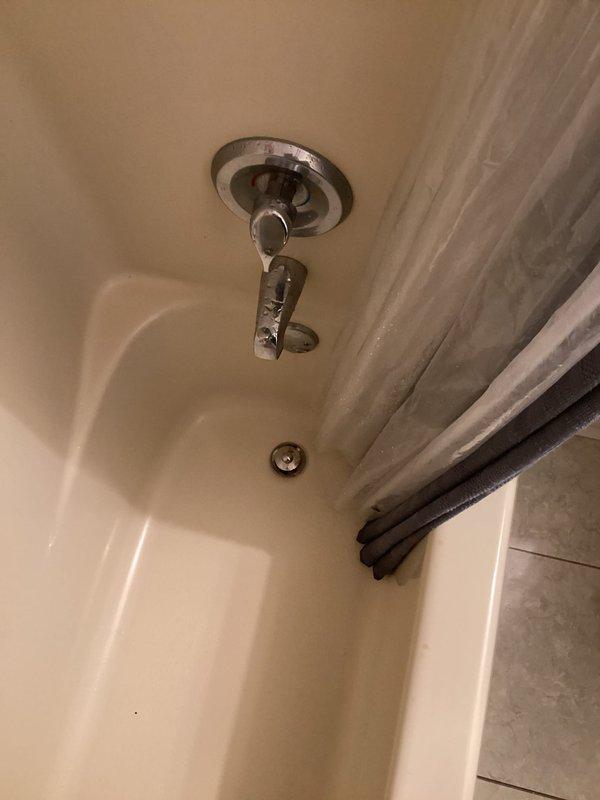 Responded to water damage complaint affecting ceiling below second-floor bathroom. Upon inspection, discovered active moisture intrusion and dripping originating from bathroom area above damaged ceiling. Homeowner had already opened ceiling to expose extent of damage, revealing significant mold growth within wall cavity behind bathtub surround. Inspected bathroom fixtures including shower valve, showerhead assembly, tub spout, and overflow drain for potential leak sources. Documented conditions with photographs showing bathtub installation and exposed wall cavity with visible mold contamination. Confirmed moisture presence and active water intrusion requiring immediate attention. Advised homeowner that mold remediation specialist would need to address biological growth before plumbing repairs could proceed. Identified bathroom plumbing system as source of water damage requiring further investigation once remediation complete.