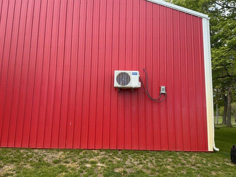 Provided estimate for completing installation of customer-supplied Mr Cool mini split system in barn structure consisting of one outdoor and one indoor unit. System requires refrigerant line set installation, electrical power connection to indoor unit, and professional startup service. Indoor unit mounted on interior plywood wall accessible via step ladder, outdoor unit installed on exterior red metal siding with electrical disconnect box in place.