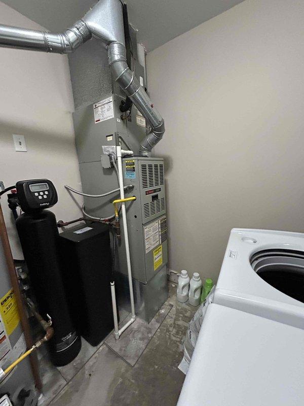 Conducted initial diagnostic assessment of existing HVAC system and returned for comprehensive evaluation to provide equipment replacement estimate. Documented current furnace installation in utility room with water treatment system and adjacent evaporator coil unit installed in wall cavity, noting refrigerant line configuration and overall system layout for replacement planning purposes.