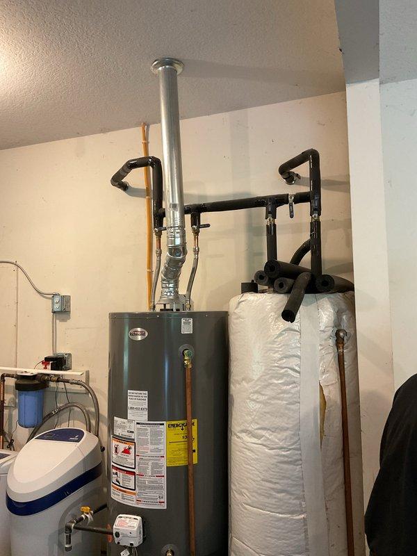 Conducted plumbing estimate for gas water heater venting installation to replace existing electric unit in residential mechanical room. Assessed attic space and structural framing to determine proper flue pipe routing through ceiling joists and roof penetration. Evaluated existing dual water heater configuration including gas-fired unit and insulated storage tank for geothermal system, along with water filtration equipment, to provide comprehensive venting solution and ensure code-compliant installation for converted gas appliance.