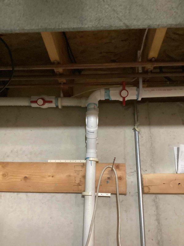 Installed sump pump system with white PVC discharge piping in basement utility area per customer specifications. Configured vertical discharge line from sump pit with proper fittings and cleanout access, secured horizontal pipe runs along ceiling joists using appropriate hangers and support clamps, and completed electrical connections for pump operation.