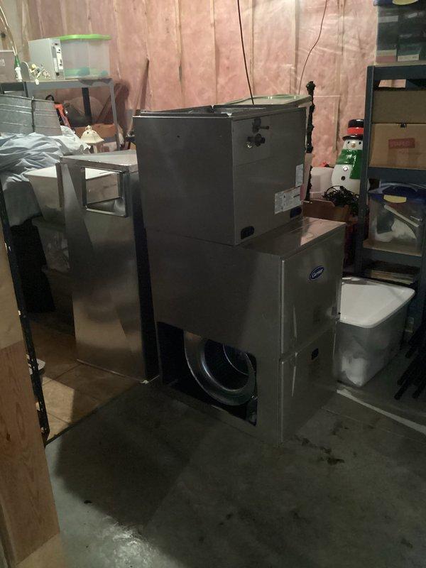 Completed full HVAC system installation in residential basement mechanical room. Installed new Carrier brand furnace unit with proper venting configuration using white PVC intake and exhaust pipes routed vertically through structure. Mounted silver air handler unit on concrete floor with evaporator coil assembly positioned above handler. Connected gray metal supply plenum and ductwork transitions to distribution system. Ran yellow flexible gas line to furnace per code requirements. Installed tall gray metal return air ductwork component for proper air circulation. Secured all manufacturer labels and documentation to equipment faces for reference. Verified all electrical connections and wiring terminations. Tested system startup sequence and confirmed proper operation of all components. System commissioned and left in full operational status providing heating and cooling capacity to residence.