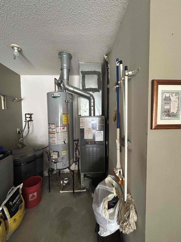 Conducted on-site assessment of existing 25-year-old Trane HVAC system for complete gas furnace and air conditioning replacement estimate. Evaluated current furnace unit located in utility room, documenting existing equipment configuration, ductwork connections, and installation parameters. Photographed existing mechanical systems including furnace positioning, metal ductwork routing from unit to ceiling, and surrounding utility room layout to determine replacement specifications. Assessed electrical connections, gas line access, condensate drainage requirements, and available clearances for new equipment installation. Evaluated existing ductwork condition and connections to determine compatibility with replacement system. Documented water heater proximity and PVC plumbing lines along walls to ensure proper clearances and code compliance for new furnace installation. Prepared comprehensive replacement estimate for complete gas furnace and air conditioning system upgrade.