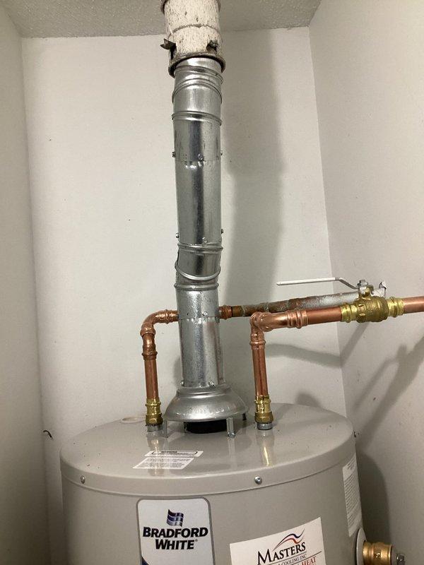 Completed installation of a Bradford White tanked gas water heater in residential utility room. Removed existing water heater unit and installed new tank with proper copper piping connections, brass shut-off valves, and compression fittings at inlet and outlet ports. Configured galvanized metal vent pipe system with insulated ductwork penetrating through ceiling for proper exhaust ventilation. Installed pressure relief valve, drain valve, and leveling supports at base of unit. All plumbing connections soldered and secured to manufacturer specifications. Obtained and completed installation under proper permitting. System tested and verified operational upon completion.