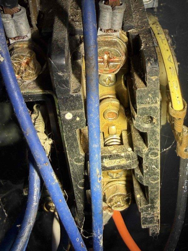 Completed comprehensive cooling system maintenance on residential air conditioning unit. Performed standard preventative maintenance procedures including inspection of outdoor condenser unit, electrical connections, and wiring components. Inspected electrical terminal block and bus bar connections, noting corrosion and weathering on brass components and accumulated debris on wiring and internal electrical connections. Verified proper operation of cylindrical condenser unit with top discharge grille, checked electrical disconnect box functionality, and ensured unit was operating within normal parameters on concrete pad with adequate clearance from surrounding landscaping.