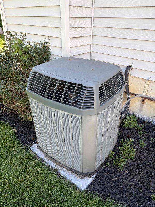 Completed comprehensive cooling system maintenance on residential air conditioning unit. Performed standard preventative maintenance procedures including inspection of outdoor condenser unit, electrical connections, and wiring components. Inspected electrical terminal block and bus bar connections, noting corrosion and weathering on brass components and accumulated debris on wiring and internal electrical connections. Verified proper operation of cylindrical condenser unit with top discharge grille, checked electrical disconnect box functionality, and ensured unit was operating within normal parameters on concrete pad with adequate clearance from surrounding landscaping.