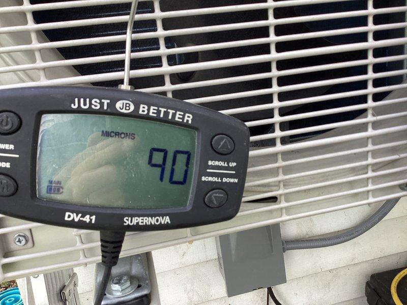 Returned to complete refrigerant charge adjustment on backup heat pump system that requires R32 refrigerant. System was previously serviced but charge could not be properly dialed in due to cold ambient temperatures below 65°F. With warmer weather conditions now present, performed vacuum test showing system holding at 90 microns, confirming system integrity. Proceeded to add R32 refrigerant and dialed in charge to manufacturer specifications for optimal system performance.