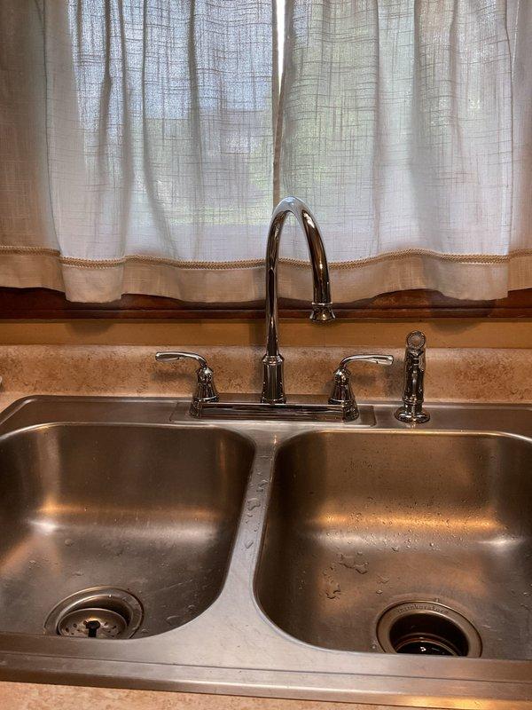 Installed customer-supplied kitchen faucet in double-basin stainless steel sink, replacing existing fixture with new chrome dual-handle faucet and spray nozzle assembly. Verified proper water supply connections, tested for leaks, and confirmed full operational functionality of both hot and cold water lines and spray attachment.