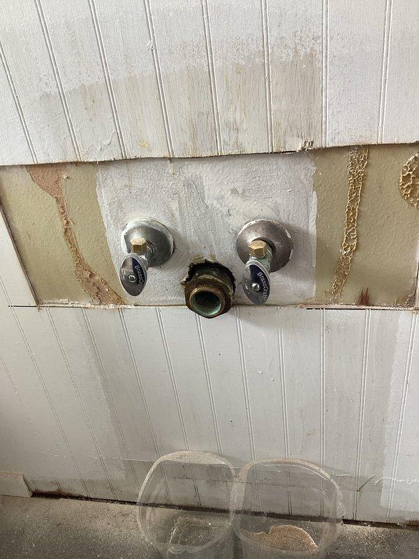 Responded to water leak investigation with vanity already removed by client. Accessed wall cavity to locate source of leak behind three-handle tub/shower valve assembly. Identified corroded copper supply piping at 90-degree elbow joint showing extensive verdigris oxidation and active leak point. Removed deteriorated section of copper pipe and fittings. Installed new copper pipe and elbow joint with proper soldered connections. Pressure tested repair to verify leak elimination. Wall showed significant water damage with rust staining around fixture mounting area, indicating prolonged moisture exposure. Documented pre-existing conditions including corroded plumbing, water-damaged beadboard paneling, and moisture staining on concrete floor. Repair completed successfully with no active leaks detected upon final inspection.
