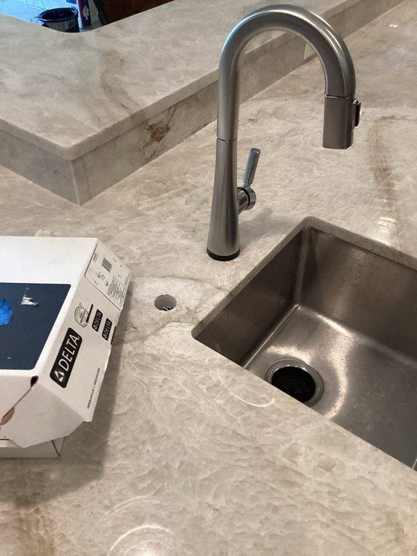 Completed installation of reverse osmosis faucet and soap dispenser on marble countertop with undermount stainless steel sink. Connected all supply lines, flex lines, and RO system components under sink, including blue shutoff valve on white PVC line and braided stainless connections to ensure proper water flow and system functionality.