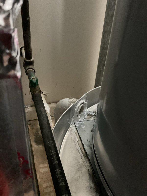 Responded to emergency call for leaking pressure relief valve on water heater causing water damage to carpet with concerns about leakage into unit below. Upon inspection, found active leak at temperature and pressure relief valve on aging water heater unit located in utility room. Documented existing conditions showing deteriorated equipment, accumulated debris, and wet flooring. Assessed valve malfunction and water heater control system to determine source of leak and prevent further water intrusion to lower apartment.