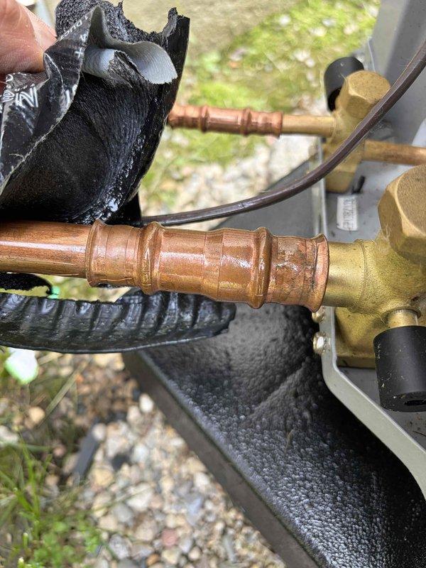 Responded to no-cooling callback for AC unit displaying 10.2 error code indicating low refrigerant. Upon inspection, identified active refrigerant leak at outdoor unit's brass valve assembly and copper line connections, evidenced by clear oil residue and visible corrosion on copper piping. Documented condition of weathered service valves, oxidized copper lines, and compromised connection points for repair authorization.