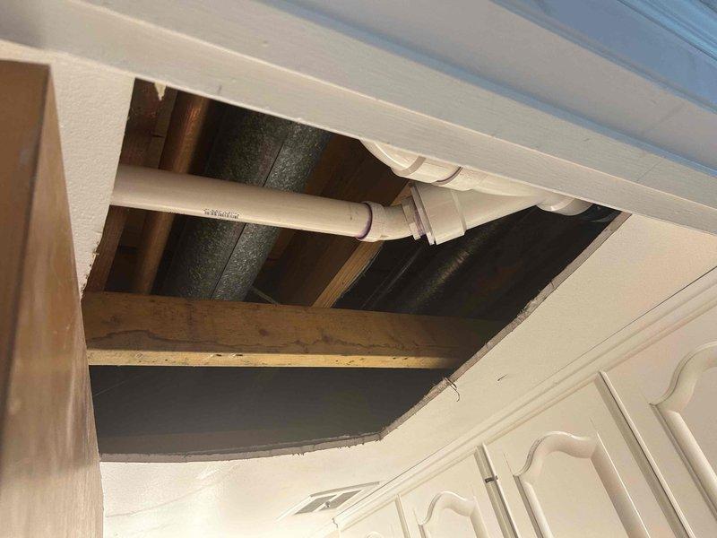 Conducted comprehensive assessment of aging HVAC system and water heating equipment for replacement estimate. Evaluated 20+ year-old air conditioning unit and 10-year-old tanked water heater, both currently operational but nearing end of service life. Inspected attic space and accessed ceiling cavity to assess existing ductwork configuration, support systems, and plumbing infrastructure. Documented metallic ductwork secured to floor joists with metal strapping, PVC plumbing lines, and structural framing conditions. Photographed installation locations and surrounding infrastructure to determine equipment replacement requirements, clearances, and access considerations for future installation work.