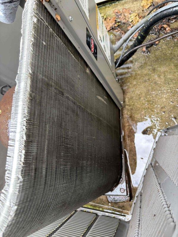 Completed first prepaid cooling maintenance visit on residential HVAC system. Performed comprehensive inspection of outdoor condensing unit, which exhibited heavy dirt and debris accumulation throughout heat exchanger coil fins, significantly restricting airflow. Documented exterior unit condition showing substantial environmental buildup, weathering, and organic matter on surrounding surfaces. Inspected indoor Lennox furnace installation and associated ductwork in basement mechanical area, verifying proper system configuration and connections. All equipment photographed for maintenance records.
