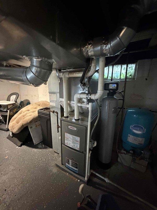Completed first prepaid cooling maintenance visit on residential HVAC system. Performed comprehensive inspection of outdoor condensing unit, which exhibited heavy dirt and debris accumulation throughout heat exchanger coil fins, significantly restricting airflow. Documented exterior unit condition showing substantial environmental buildup, weathering, and organic matter on surrounding surfaces. Inspected indoor Lennox furnace installation and associated ductwork in basement mechanical area, verifying proper system configuration and connections. All equipment photographed for maintenance records.