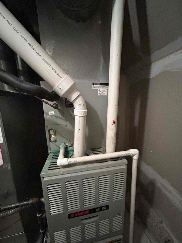 Conducted comprehensive site evaluation for dual HVAC system replacement estimate at residential property. Assessed existing outdoor condenser unit located in narrow side yard with vegetation encroachment and evaluated indoor Trane XE 90 furnace installation in utility closet, including existing PVC venting configuration and electrical connections. Documented current equipment conditions, clearance requirements, and access limitations to provide accurate replacement specifications for both heating and cooling systems.