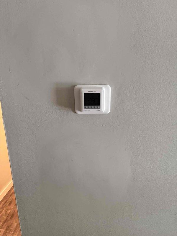 Completed full HVAC system replacement at apartment unit, removing obsolete 1.5 ton R22 ceiling-mounted fan coil and matching outdoor condenser. Installed new Carrier FMA5X2400AL 1.5 ton wall-mounted fan coil with 8kW electric strip heat and Carrier GA4SAN51800N 1.5 ton 14 SEER single-stage air conditioner utilizing R454 refrigerant. Cut open ceiling and wall sections to access existing ductwork, reconnected all duct connections, condensate drain line, and electrical power supply. Extended existing line set with additional 25' section, flushed and pressure-tested refrigerant lines for reuse. Mounted outdoor unit on new PVC pad with electrical disconnect and whip. Installed Honeywell T6 programmable thermostat for system control. Performed complete system startup, evacuated lines, charged unit to manufacturer specifications, and verified proper operation of heating and cooling modes. Removed and hauled away all old equipment from premises.