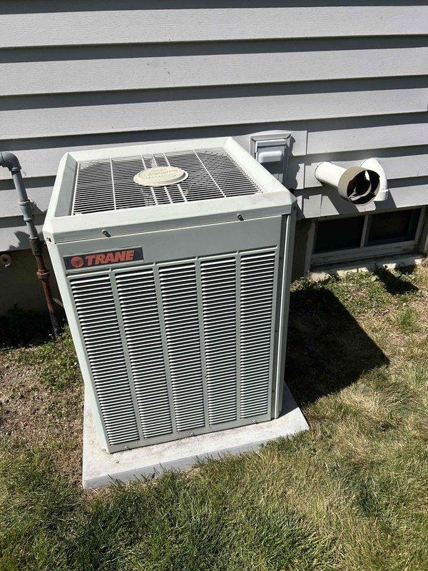 Responded to service call for AC unit freezing up. Upon inspection, documented existing HVAC system configuration including indoor XL 80 furnace unit with associated PVC vent piping and outdoor Trane condensing unit. Measured and photographed current installation setup showing horizontal PVC venting with 90-degree elbows, mounting brackets, and refrigerant line connections between indoor and outdoor components. Assessed complete system for replacement estimate, noting equipment positioning on concrete pad adjacent to building exterior with proper condensate drainage and electrical connections in place.