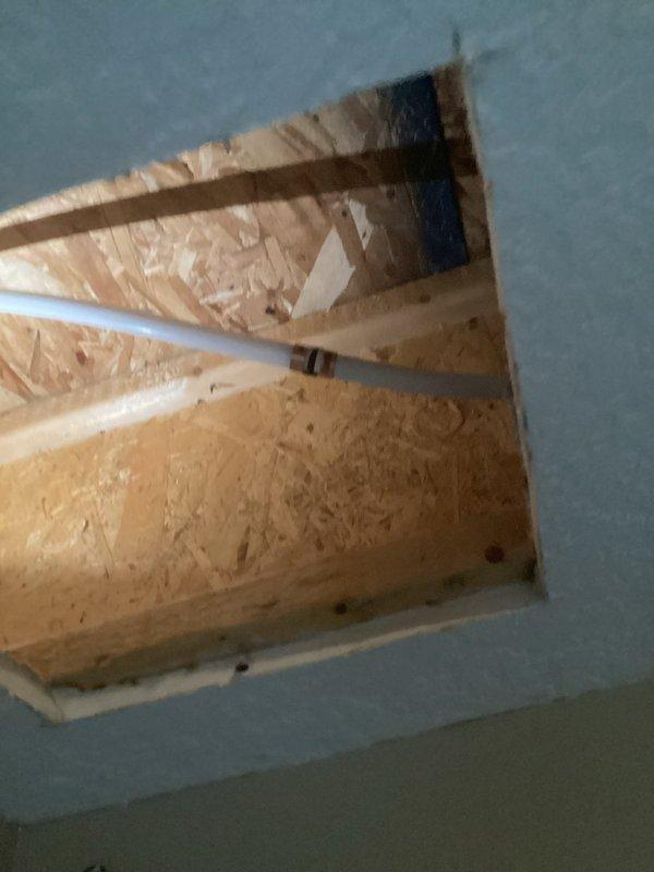 Responded to reported water leak in basement suspected to originate from outdoor water spigot. Upon investigation, accessed ceiling cavity to trace water source and inspect plumbing infrastructure. Located PVC piping running through ceiling joists with compromised penetration point showing signs of water intrusion. Identified corroded metal pipe collar at ceiling penetration as primary leak source, with visible rust and oxidation indicating prolonged moisture exposure. Created access opening in ceiling drywall to facilitate inspection and repair of affected area. Documented conditions with photographs showing extent of water damage and deteriorated pipe flange. Assessed routing of water supply line serving exterior hose bib and confirmed connection point as leak origin.