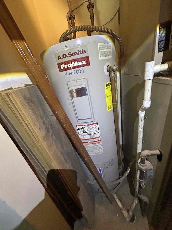 Tech lead Dennis conducted a comprehensive HVAC system evaluation for equipment replacement. Assessment included inspection of existing outdoor air conditioning condenser unit installed on concrete pad with proper electrical disconnect, and aging A.O. Smith ProMax water heater dated from 2009 located in utility area beneath staircase. Documentation through photography captured current equipment conditions, installation configurations, and surrounding service access areas to provide accurate replacement specifications and system upgrade recommendations.