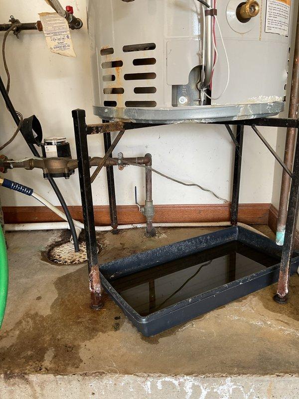 Responded to service call for leaking tanked gas water heater in garage with visible water accumulation around base and in drain pan. Upon inspection, identified active leak at bottom of unit with moisture staining on concrete floor and corrosion present on metal support frame base. Documented existing Hydrojet brand water heater installation including plumbing connections, copper piping with foam insulation, PVC venting system, and drain pan configuration. Photographed leak source, water damage extent, and overall installation condition for assessment and customer records.