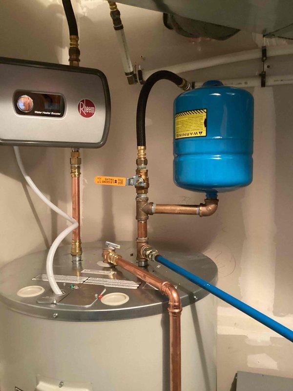 Completed installation of geothermal heat pump system with associated mechanical equipment. Installed Rheem MODEL W6B003BBN1A0210F3D10 geothermal unit with electrical service rated at 208-230V, 60Hz, requiring 36.7/44 circuit amperage and 43/46.5 minimum circuit amps. Unit manufactured in Fort Wayne, Indiana, serial number 260601319, job number 831879. Mounted and secured main heat pump unit to wall with proper specification labeling affixed for future reference and compliance documentation.

Installed complete domestic hot water system integration including Rheem electric water heater with expansion tank assembly. Mounted blue pressure/expansion tank to wall with proper support and connected via copper piping with brass fittings and compression connections. Ran copper supply and return lines from geothermal unit to water heater with appropriate shut-off valves at key connection points. Installed black flexible connector hose between plumbing manifold and water heater inlet. Connected 