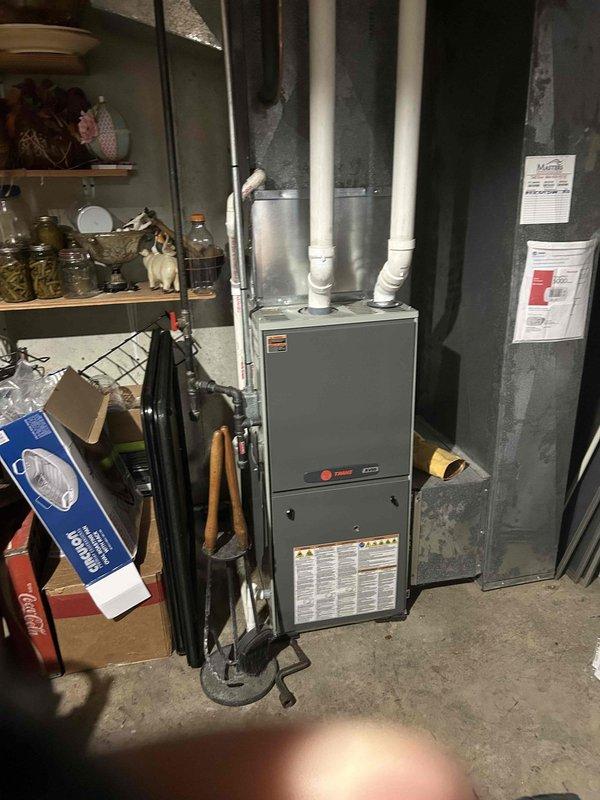 Tech lead Dennis conducted an HVAC system evaluation for equipment replacement in a basement mechanical room. Assessment included a Trane furnace unit with dual PVC vent pipes, measuring existing equipment dimensions and documenting current installation configuration. Comprehensive photographic documentation was completed to support replacement estimate specifications and ensure proper sizing for new equipment installation.