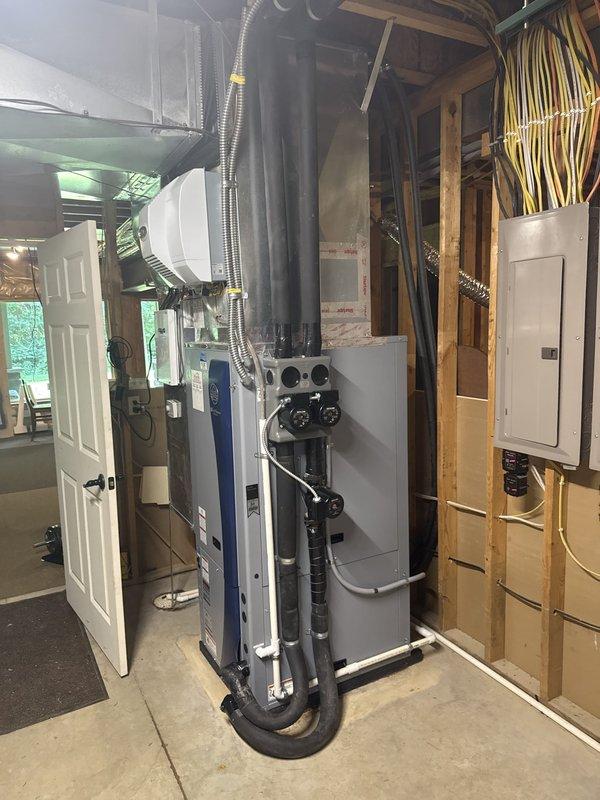 Completed installation of residential geothermal HVAC system in basement utility area. Installed vertical air handler unit with integrated humidifier system and connected all necessary ductwork using metal flex ducting and rigid duct runs. Mounted and wired electrical junction boxes and breaker panel to code specifications, running conduit and electrical wiring throughout the mechanical room to power all system components. Connected geothermal heat pump unit with proper refrigerant lines and manifold piping. Installed water heater/buffer tank with multiple black PEX piping connections running to floor penetrations for ground loop integration. Routed all copper plumbing lines along wall framing for hydronic distribution. Secured all flex conduit, wiring bundles, and mechanical connections according to manufacturer specifications. Verified proper clearances around all equipment for service access and code compliance. System tested and confirmed operational with all electrical connections