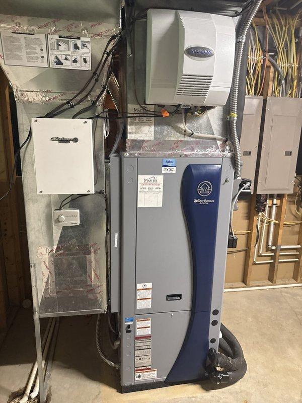 Completed installation of residential geothermal HVAC system in basement utility area. Installed vertical air handler unit with integrated humidifier system and connected all necessary ductwork using metal flex ducting and rigid duct runs. Mounted and wired electrical junction boxes and breaker panel to code specifications, running conduit and electrical wiring throughout the mechanical room to power all system components. Connected geothermal heat pump unit with proper refrigerant lines and manifold piping. Installed water heater/buffer tank with multiple black PEX piping connections running to floor penetrations for ground loop integration. Routed all copper plumbing lines along wall framing for hydronic distribution. Secured all flex conduit, wiring bundles, and mechanical connections according to manufacturer specifications. Verified proper clearances around all equipment for service access and code compliance. System tested and confirmed operational with all electrical connections