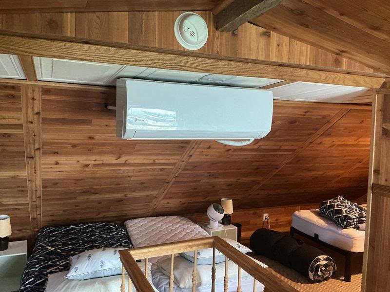 Completed site assessment for mini split installation in attic loft bedroom with sloped wood-paneled ceilings and exposed beam construction. Evaluated existing ceiling-mounted ductless mini split unit and documented current system configuration, mounting hardware, and spatial requirements for potential equipment upgrade or replacement.