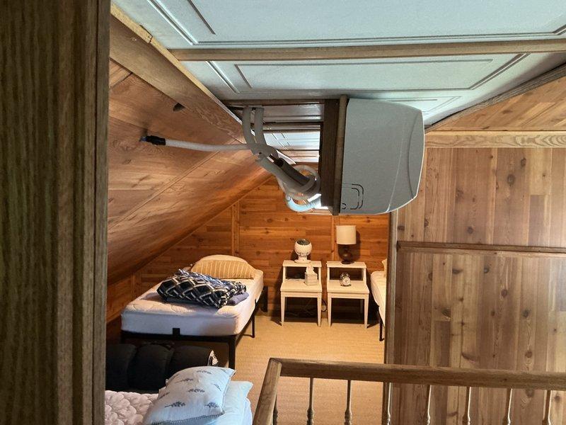 Completed site assessment for mini split installation in attic loft bedroom with sloped wood-paneled ceilings and exposed beam construction. Evaluated existing ceiling-mounted ductless mini split unit and documented current system configuration, mounting hardware, and spatial requirements for potential equipment upgrade or replacement.
