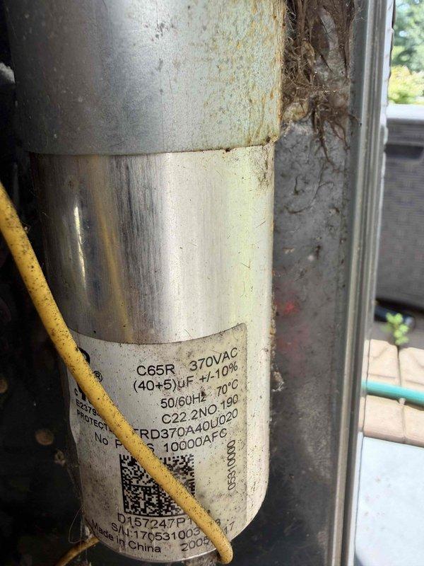 Completed comprehensive air conditioning tune-up including inspection of cooling system components and shared furnace elements. Inspected dual-run capacitor showing signs of weathering and oxidation on exterior casing; verified electrical specifications at 370VAC with 40+5 μF ratings remain within operational parameters. Cleared extensive debris accumulation including dirt, plant matter, and organic material from condensate lines and surrounding compartment to restore proper airflow and drainage.