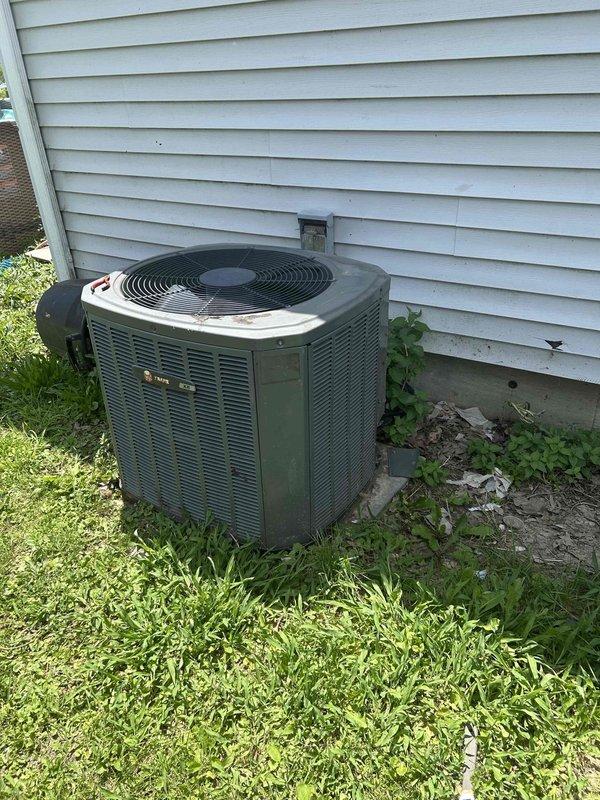 Assessed existing R-22 air conditioning system with confirmed refrigerant leak at outdoor condenser unit. Evaluated Trane condenser positioned on ground-level pad with vegetation growth impacting clearance requirements. Documented system configuration with furnace located in main floor laundry room to remain in service. Provided replacement estimate for new air conditioning system while retaining existing heating equipment, discussed financing options, and coordinated follow-up contact through designated family representative for approval and scheduling.