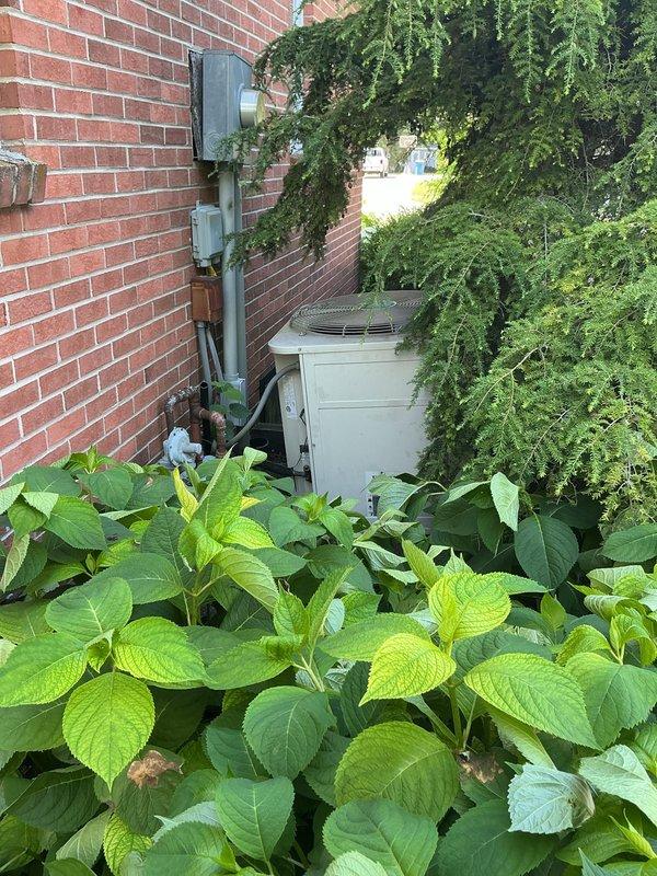 Completed on-site evaluation for HVAC system replacement, assessing both outdoor condensing unit and indoor furnace/air handler configuration. Exterior unit positioned against brick wall in landscaped area with existing electrical service connections; indoor equipment consists of vertical-stacked Plus 90t furnace with air handler and established PVC condensate drainage system. Documented current system specifications and installation conditions through photographic assessment to provide comprehensive replacement equipment recommendations and installation requirements.