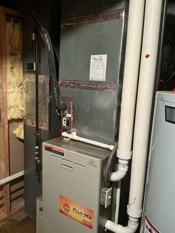 Completed on-site evaluation for HVAC system replacement, assessing both outdoor condensing unit and indoor furnace/air handler configuration. Exterior unit positioned against brick wall in landscaped area with existing electrical service connections; indoor equipment consists of vertical-stacked Plus 90t furnace with air handler and established PVC condensate drainage system. Documented current system specifications and installation conditions through photographic assessment to provide comprehensive replacement equipment recommendations and installation requirements.