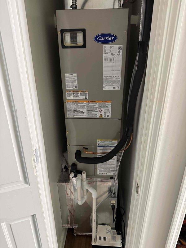 Completed full HVAC system installation including outdoor Carrier condensing unit and indoor air handler with evaporator coil. Installed condensing unit on prepared gravel pad with proper clearances, ran electrical whip to wall-mounted disconnect, and established refrigerant line connections. Mounted air handler vertically in side closet with PVC condensate drain lines and auxiliary drain pan assembly. Removed old equipment from site and delivered to maintenance office per work order specifications.