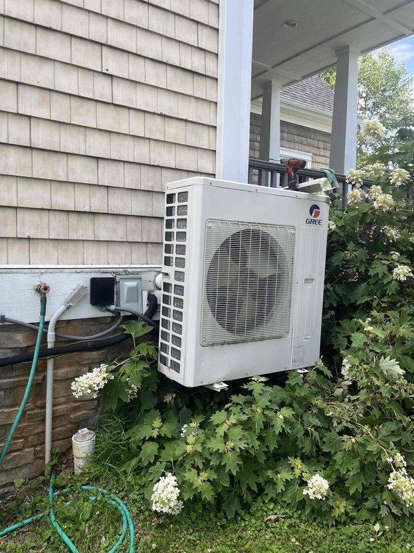 Responded to no cooling complaint on Gree ductless mini-split system serving upstairs south-facing bedroom. Upon inspection, found 10+ year old wall-mounted air handler and outdoor condenser unit with significant vegetation overgrowth restricting airflow to condenser. Unit displayed operational indicator lights but was not achieving adequate cooling capacity. Cleared hydrangea bushes and excess foliage from around condenser to restore proper airflow and ventilation clearances. Verified system operation and cooling performance after clearing obstruction. Addressed customer inquiry regarding why ductless units were installed in home with existing central air system; explained that mini-splits provide supplemental zone cooling for rooms with high heat gain or inadequate coverage from central system, particularly common for south-facing bedrooms with solar heat load.