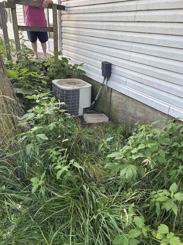 Tech lead Larry completed an HVAC system replacement estimate, documenting the existing indoor air handler unit showing significant wear and surface contamination, along with the outdoor condensing unit situated in an overgrown area with inadequate clearance from surrounding vegetation. The assessment included photographic documentation of both components to support replacement recommendations, noting the compromised serviceability due to environmental conditions and equipment age.