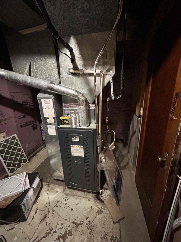 Tech lead conducted comprehensive assessment of existing HVAC system for complete replacement estimate. Documented current furnace installation in basement mechanical room, including measurements of confined equipment space and existing ductwork configuration. Evaluated condition of aging furnace unit, metal supply ductwork with reflective insulation, and associated mechanical components including condensate drainage lines and electrical connections. Photographed equipment access clearances, ceiling-mounted distribution systems, and spatial constraints within utility area to determine proper sizing and installation requirements for replacement system. Assessed existing infrastructure condition including corroded access panels, water staining on metallic surfaces, and overall equipment deterioration to provide accurate replacement specifications and scope of work for complete HVAC system upgrade.