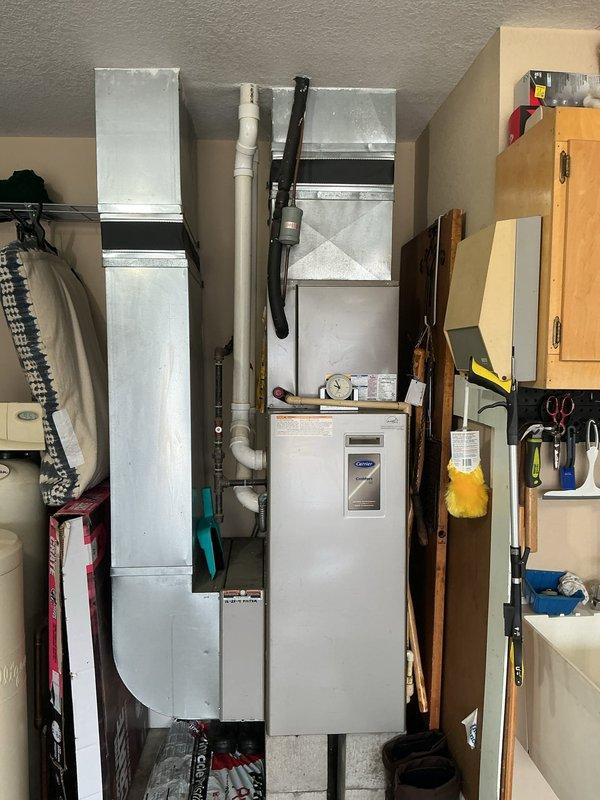 Conducted on-site evaluation for complete HVAC system replacement following initial no-cool service call that was temporarily resolved by lead technician. Assessed existing Carrier air handler and furnace unit located in multipurpose utility closet with limited clearance. Documented equipment dimensions and spatial constraints, including surrounding ductwork configuration with galvanized metal rectangular ducts and white PVC piping. Photographed current installation showing standard residential HVAC setup with warning labels visible on gas-fired equipment. Evaluated accessibility challenges due to shared storage space with household items and measured equipment dimensions for replacement sizing. Prepared comprehensive estimate for furnace and air conditioning system replacement at primary residence. Additional estimate requested for separate lake house property to install new air conditioning system.