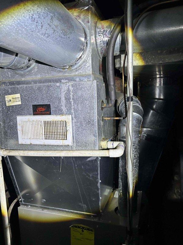 Completed estimate for complete HVAC system replacement at residential property. Existing air conditioning system was deemed non-functional by previous service provider with assessment that unit would not survive the cooling season. Evaluated basement-located furnace and indoor air handler unit, as well as outdoor condensing unit. Documented current system configuration including gray air handler with return air grille, ductwork showing condensation issues, electrical connections, and associated heating components in basement utility area. Assessed outdoor condenser unit positioned on concrete pad along building exterior with refrigerant lines and conduit running to structure through gravel landscape bed. Photographed complete system setup to provide comprehensive documentation for replacement proposal.