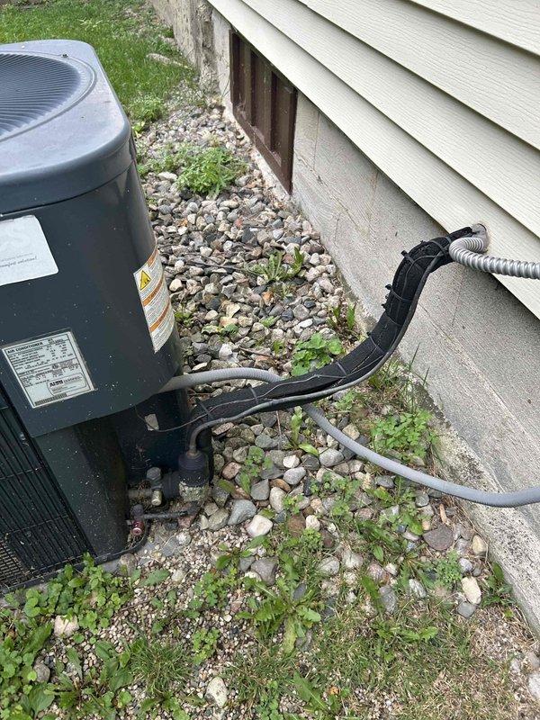 Completed estimate for complete HVAC system replacement at residential property. Existing air conditioning system was deemed non-functional by previous service provider with assessment that unit would not survive the cooling season. Evaluated basement-located furnace and indoor air handler unit, as well as outdoor condensing unit. Documented current system configuration including gray air handler with return air grille, ductwork showing condensation issues, electrical connections, and associated heating components in basement utility area. Assessed outdoor condenser unit positioned on concrete pad along building exterior with refrigerant lines and conduit running to structure through gravel landscape bed. Photographed complete system setup to provide comprehensive documentation for replacement proposal.