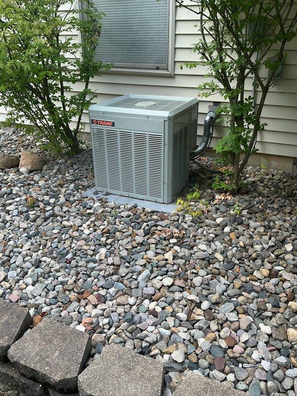 Completed comprehensive evaluation of existing Trane air conditioning system experiencing no cooling condition. Assessed outdoor condensing unit positioned on concrete pad with surrounding landscaping, noting operational failure requiring full system replacement. Documented equipment dimensions and current installation configuration, including existing electrical and refrigerant line routing along exterior wall. Observed corrosion on cylindrical component mounting, indicating age-related deterioration of system. Provided replacement options and recommendations for new AC unit installation to restore cooling capacity to residence.