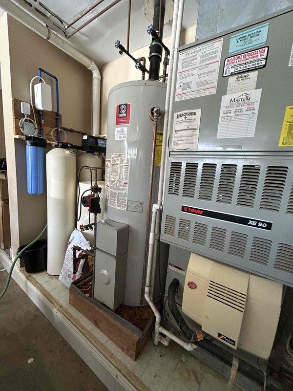Provided estimate for complete HVAC system replacement in garage area, including gas furnace and air conditioning unit to replace existing Trane XE90 furnace system that appears to be original to the home. Assessed current equipment configuration and available space in utility area shared with water heater and existing water filtration system. Discussed options for optimizing installation space, including potential tankless water heater conversion to accommodate new HVAC equipment. Additionally evaluated water quality concerns and provided recommendations for reverse osmosis system installation to replace current water treatment setup. Documented existing mechanical room layout with gas lines, electrical panel, ductwork, and plumbing connections to determine proper sizing and placement for replacement equipment in larger residential lake property.