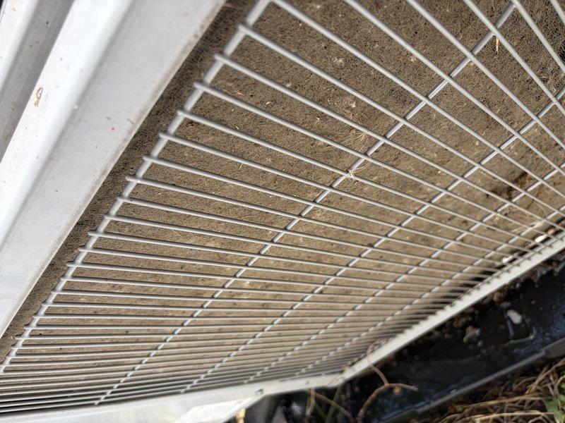 Responded to no cooling complaint on system installed less than one year ago. Upon arrival, inspected outdoor condensing unit and found excessive dirt and debris accumulation on condenser coil and grille assembly, restricting airflow. Cleaned condenser coil and surrounding components, removed obstructions from grille openings, and verified proper airflow restoration. System returned to normal cooling operation with adequate airflow through condenser unit.