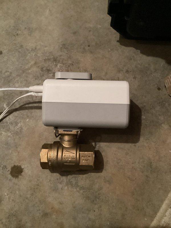 Installed motorized ball valve assembly with electric actuator in basement utility area. Mounted wall control unit with indicator light and completed electrical connections. Valve positioned to integrate with existing sump pump system for automated water flow control.