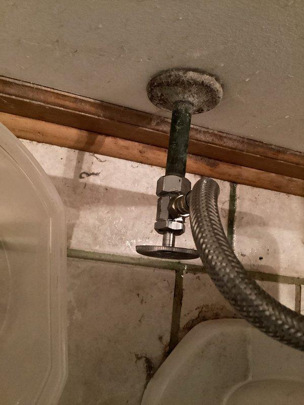 Responded to service call for leaking shut-off valve and continuously running toilet. Upon inspection, identified active leak at the connection point between the toilet supply shut-off valve and the wall supply line, occurring before the pipe enters the wall. Valve assembly showed significant accumulation of debris and age-related wear. Additionally diagnosed toilet fill valve malfunction causing continuous water flow into tank. Documented existing conditions with photographs showing corroded valve hardware, braided supply line connections, and overall plumbing configuration. Temporary containment vessel was in place beneath leak point upon arrival to prevent water damage.