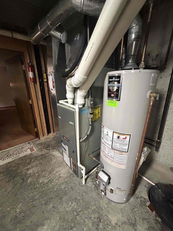 Tech lead Alex conducted a comprehensive HVAC system evaluation for equipment replacement. Assessment included inspection of the existing outdoor air conditioning condenser unit installed on a concrete pad against the building's exterior, as well as the indoor furnace system located in the basement mechanical room alongside the water heater. Detailed photographic documentation was captured of both the exterior condensing unit with its current installation configuration and the interior furnace with associated ductwork and PVC venting systems to support replacement specifications and planning.