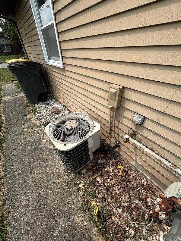 Conducted comprehensive site evaluation of existing residential HVAC system under tech lead supervision. Documented current air conditioning condenser unit installation, including equipment placement on concrete pad with white decorative stone surround for proper drainage. Assessed exterior-mounted electrical components, conduit routing, and junction box configuration along vinyl siding. Evaluated copper refrigerant line runs from condenser to building penetration point. Photographed equipment positioning relative to property boundaries, walkways, and utility access points to determine optimal replacement unit placement and clearance requirements. Prepared detailed estimate for complete system replacement based on existing installation conditions and site constraints.